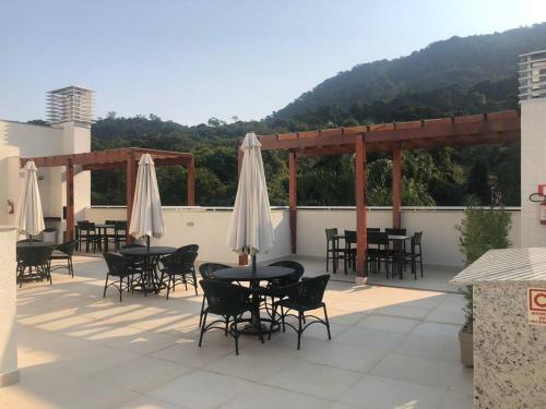 a patio with tables and chairs and white umbrellas at Apartamento aconchegante na Praia in Ubatuba