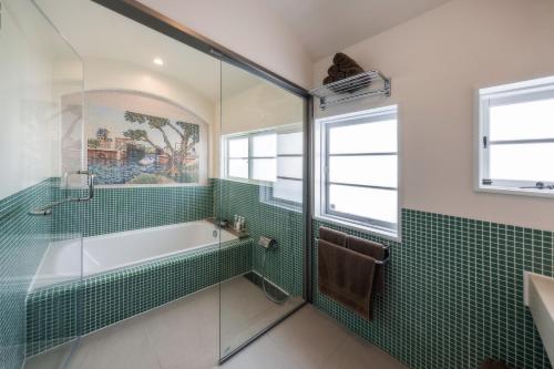 a bathroom with a tub and green tile at 源泉かけ流しの一棟貸し温泉宿The Feet Dogo in Matsuyama