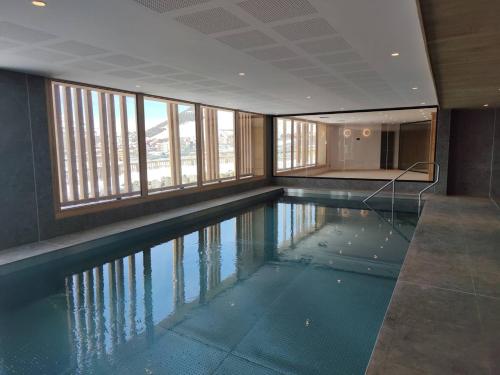 - une grande piscine dans un bâtiment doté de fenêtres dans l'établissement Coup de coeur ski aux pieds avec piscine, spa, et fitness, à L'Alpe-d'Huez