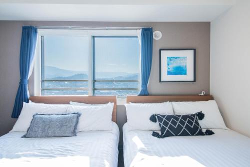 a bedroom with two beds with blue curtains and a window at GREE in Otaru