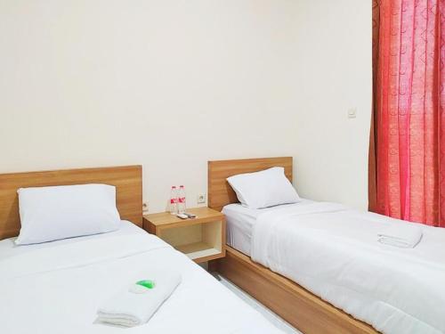 two beds in a room with white walls and red curtains at Zumo Home Tegal Mitra RedDoorz in Tegal