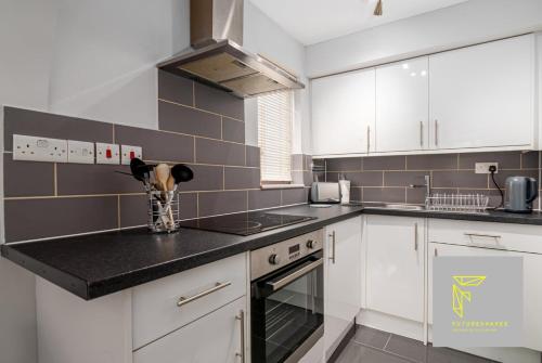 a kitchen with white cabinets and black counter tops at GuestReady - Cosy Wimbledon Studio Flat in London
