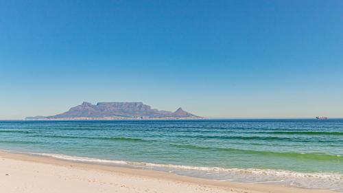 a view of the beach with an island in the distance at Beachfront Apartment with wrap around terrace in Blouberg, 04 Azul in Bloubergstrand