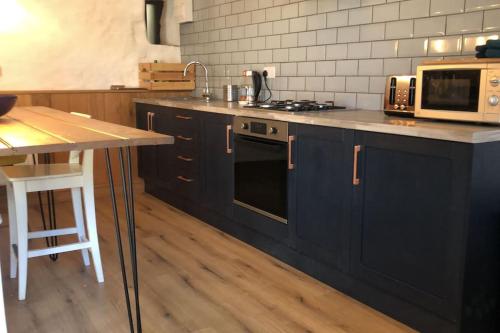 a kitchen with navy blue cabinets and a microwave at The Milking Parlour at Berthllwyd in Quakers Yard