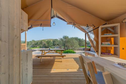 eine Holzterrasse mit einem Picknicktisch in einem Zelt in der Unterkunft Adriatic Heritage Glamping No2 with Jacuzzi in Donje Selo na Šolti