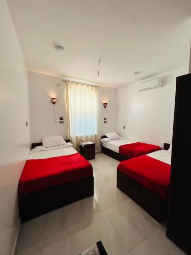 two beds in a hotel room with red sheets at ANA-KA Guest house in Aswan