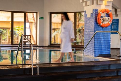 a woman in a white dress walking by a swimming pool at Vila Gale Isla Canela in Isla Canela
