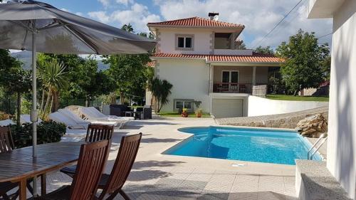 a house with a swimming pool and an umbrella at Beautiful detached villa with private pool, Fibre Wi-fi, garden, games room & BBQ in Terras de Bouro