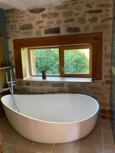 une grande baignoire blanche dans une salle de bain avec une fenêtre dans l'établissement Maison dans la campagne bretonne, à Glomel