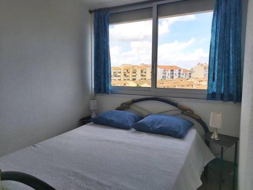 une chambre avec un lit avec des oreillers bleus et une fenêtre dans l'établissement Appartement proche du Casino et Séquarium, au Grau-du-Roi