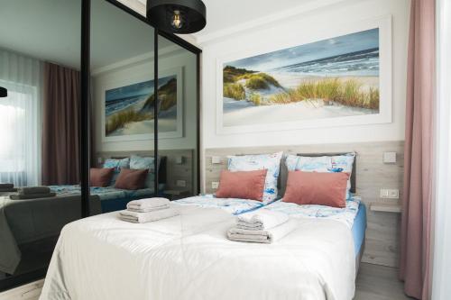 a bedroom with a bed with white sheets and pink pillows at SUNSET RESORT APARTAMENT KaPi in Grzybowo