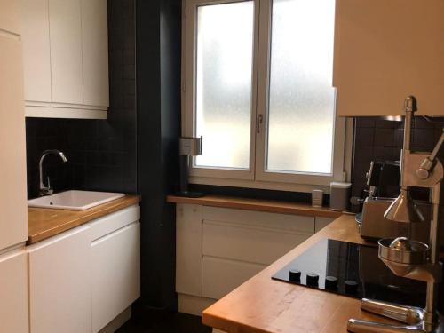 une cuisine avec des armoires blanches, un évier et une fenêtre dans l'établissement 60sqm design apartment with stunning view, à Paris