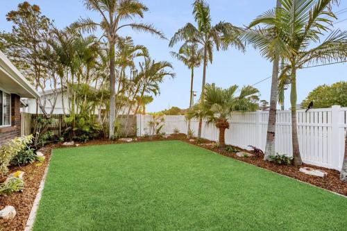 a yard with palm trees and a white fence at Caba Bliss - Walk to Cabarita Beach! in Cabarita Beach