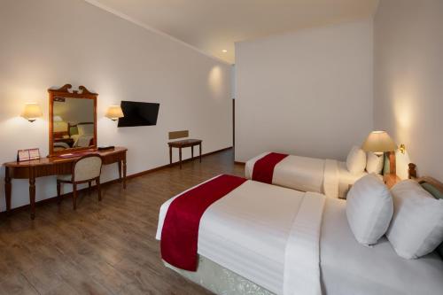 a hotel room with two beds and a desk and a mirror at Sinabung Hills Berastagi in Berastagi