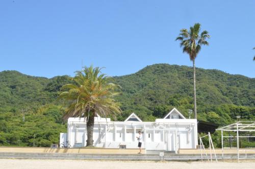 un homme debout devant une maison blanche avec un palmier dans l'établissement アグリート島時間, à Onomichi