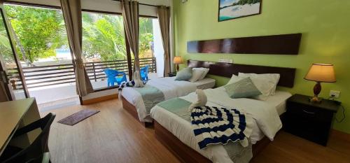 two beds in a room with green walls and windows at Liberty Guesthouse Maldives in Mahibadhoo