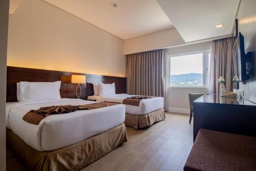 a hotel room with two beds and a desk at Harolds Hotel Cebu in Cebu City