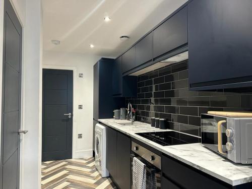 a kitchen with black cabinets and a stove top oven at City Centre Apartments - 1 Bed Apartments - 5 Min Walk from Train Station - Designed for Professionals - Free WiFi - Full Kitchen - Sofa Bed - Ideal for Long Work Stays in Peterborough