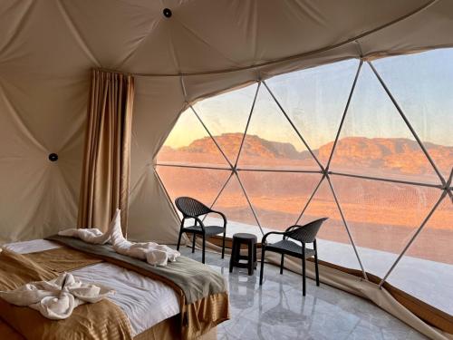 a tent with two chairs and a bed and a large window at Shaheen Camp Wadi rum in Wadi Rum