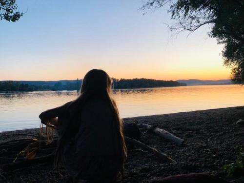 a woman sitting on the shore of a body of water at Repülőhal Apartmanház in Zebegény