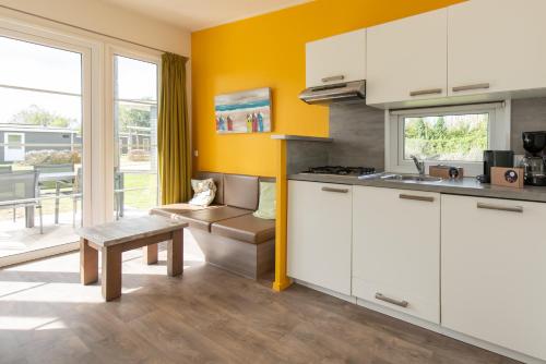 a kitchen with white cabinets and a couch and a table at Kompas Camping Nieuwpoort in Nieuwpoort