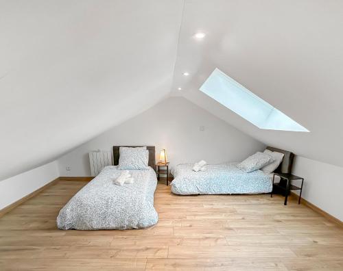 deux lits dans une chambre mansardée avec une lucarne dans l'établissement Maison lumineuse avec verrière & grand écran, à Saint-Leu-dʼEsserent