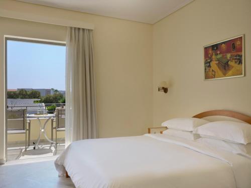 a white bedroom with a large bed and a balcony at Atlantica Yakinthos in Kato Daratso