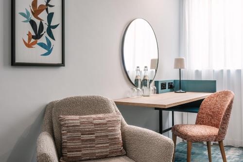 a room with a desk with a chair and a mirror at voco Winchester Hotel & Spa by IHG in Winchester