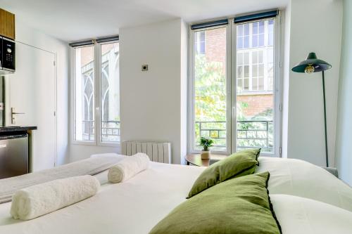 - un lit blanc avec des oreillers verts dans une chambre dotée de fenêtres dans l'établissement Montmartre l Center & Historic Sacré-Coeur, à Paris