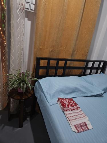 ein Bett mit einer blauen Decke und einem Tisch mit einer Pflanze in der Unterkunft California Nest in Tezpur