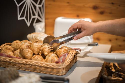 a person holding a pair of tongs over a basket of bread at COOEE alpin Hotel Kitzbüheler Alpen in Sankt Johann in Tirol
