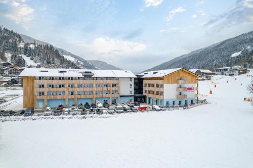 a building in the snow with chairs in front of it at COOEE alpin Hotel Bad Kleinkirchheim in Bad Kleinkirchheim