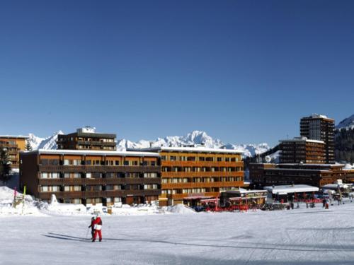 une personne à skis dans la neige devant les bâtiments dans l'établissement Joli studio rénové pour 4, au pied des pistes, balcon, cuisine équipée, non fumeur - FR-1-455-235, à La Plagne Tarentaise