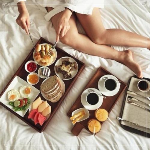 a woman sitting on a bed with a tray of food at Bantique Hotel in Da Nang
