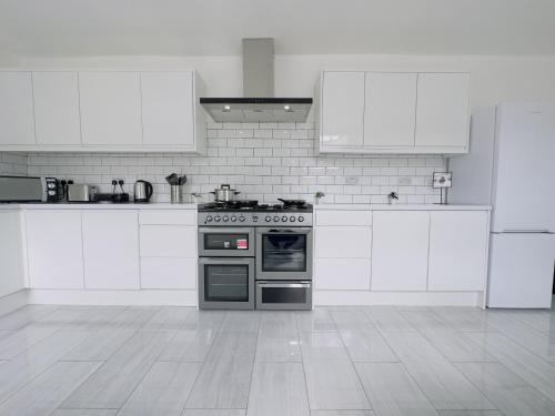 a white kitchen with a stove and white cabinets at Leyton House - SleepyLodge in London
