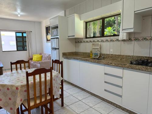 a kitchen with white cabinets and a table and a dining room at Residencial Vista Bela in Bombinhas