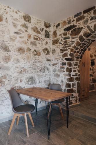 a wooden table and two chairs against a stone wall at Lefteris Rooms in Kámbos