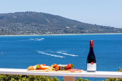 a bottle of wine and a plate of food next to the ocean at The Peak of Mt Martha Spa and Sunset Views in Mount Martha