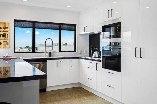 a white kitchen with white cabinets and black appliances at Awesome Designer 3BR Apt in the Heart of Manukau in Auckland