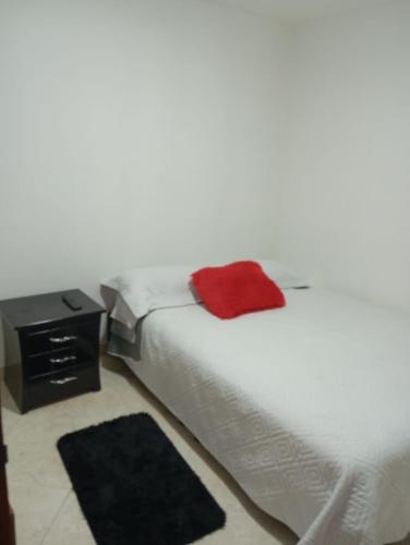 a white bed with a red pillow on top of it at Hospedaje BOGOTA cerca al aeropuerto in Bogotá