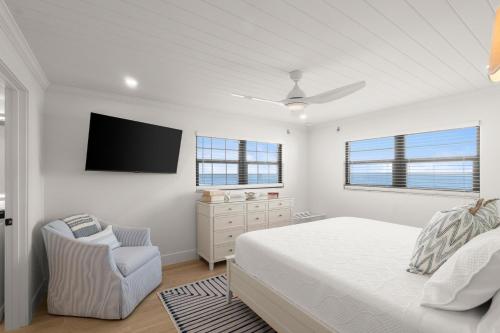 a white bedroom with a bed and a chair at Serenity Shores Renovated Top Floor Condo w Stunning Ocean Views in New Smyrna Beach