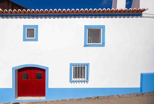 a white building with a red door and two windows at Refúgio Alentejano in Alandroal