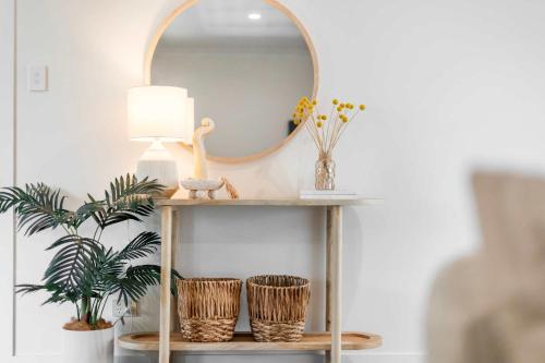 a console table with a mirror and wicker baskets at Coastal Calm - Oceanstays in Yamba