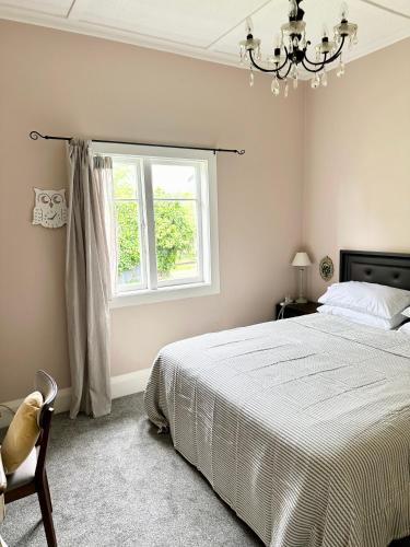 a bedroom with a bed and a window and a chandelier at Bycroft Lodge in Karaka