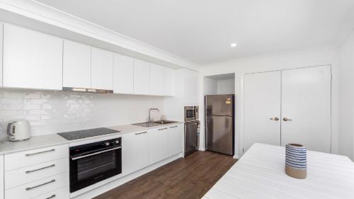 a kitchen with white cabinets and a stainless steel refrigerator at 'Coastal Harmony Cottage' by HolidayCo in Hardys Bay
