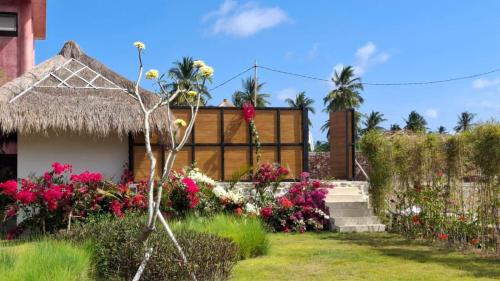 a garden with flowers and a thatch roof at Casa Samudra - charming & spacious villa by the sea surrounded by nature in Selong Belanak