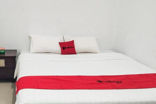 a white bed with a red pillow on it at RedDoorz Syariah at Sayang Ibu Village Nongsa Batam in Nongsa