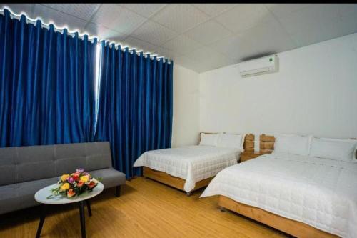 a bedroom with two beds and a couch and blue curtains at ST Homestay Tản Lĩnh - Venuestay in Mỹ Khê