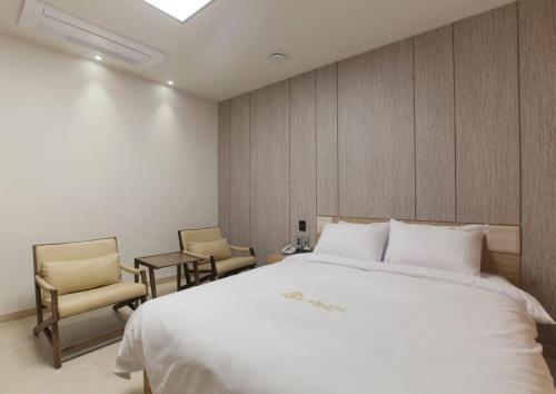 a bedroom with a large white bed and two chairs at Yeosu Stay Hotel in Yeosu