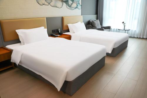 two beds in a hotel room with white sheets at 空港别墅酒店广州白云国际机场店 in Guangzhou
